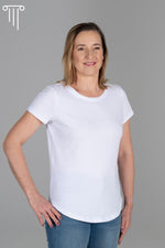 Zdjęcie przedstawia białą bawełnianą koszulkę na modelce. Koszulka ma krótkie rękawy i okrągły dekolt. Charakterystyczną cechą tej koszulki jest przedłużony przód, który dodaje jej oryginalności i dopasowania. Materiał jest miękki i przewiewny, idealny na ciepłe dni. Koszulka jest uniwersalna i nadaje się zarówno na codzienne noszenie, jak i na nieformalne spotkania. Przedłużony przód zapewnia wygodę i swobodę ruchu. Plus size