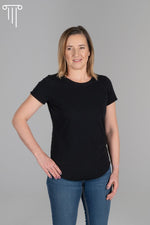 Zdjęcie przedstawia czarną bawełnianą koszulkę na modelce. Koszulka ma krótkie rękawy i okrągły dekolt. Charakterystyczną cechą tej koszulki jest przedłużony przód, który dodaje jej oryginalności i dopasowania. Materiał jest miękki i przewiewny, idealny na ciepłe dni. Koszulka jest uniwersalna i nadaje się zarówno na codzienne noszenie, jak i na nieformalne spotkania. Przedłużony przód zapewnia wygodę i swobodę ruchu. Plus size