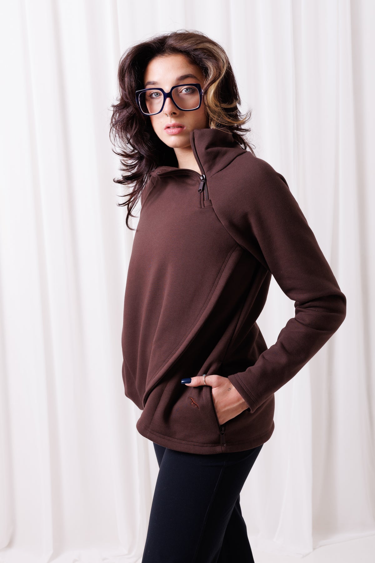 Modelka w brązowej bluzie Papaya z asymetrycznym przodem i przedłużonym tyłem, uszytej ze 100%  polskiej bawełny. Bluza ma kieszenie z zamkami.  odzież sportowa damska szyta w Polsce, Gdańsk.