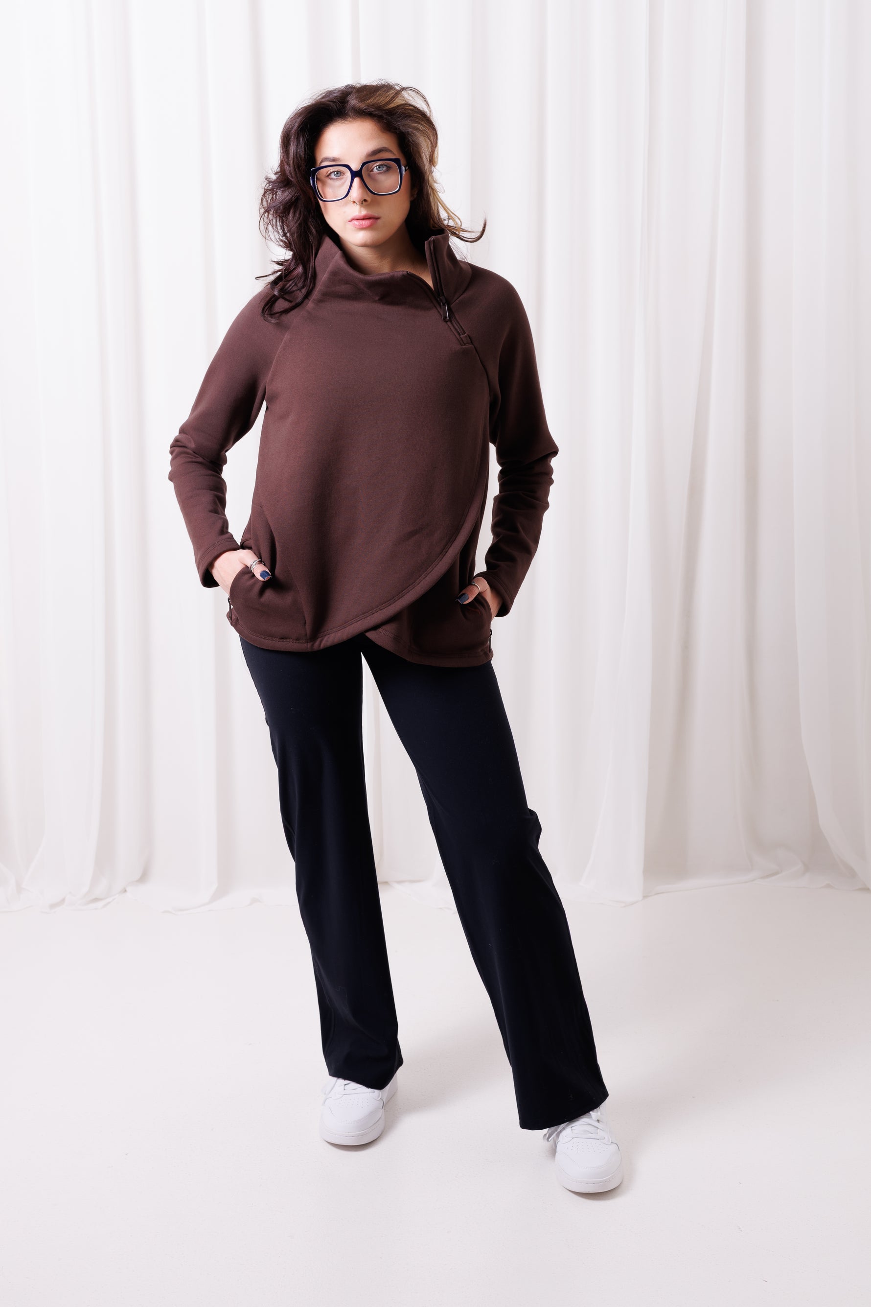 Modelka w brązowej bluzie Papaya z asymetrycznym przodem i przedłużonym tyłem, uszytej ze 100%  polskiej bawełny. Bluza ma kieszenie z zamkami.  odzież sportowa damska szyta w Polsce, Gdańsk.