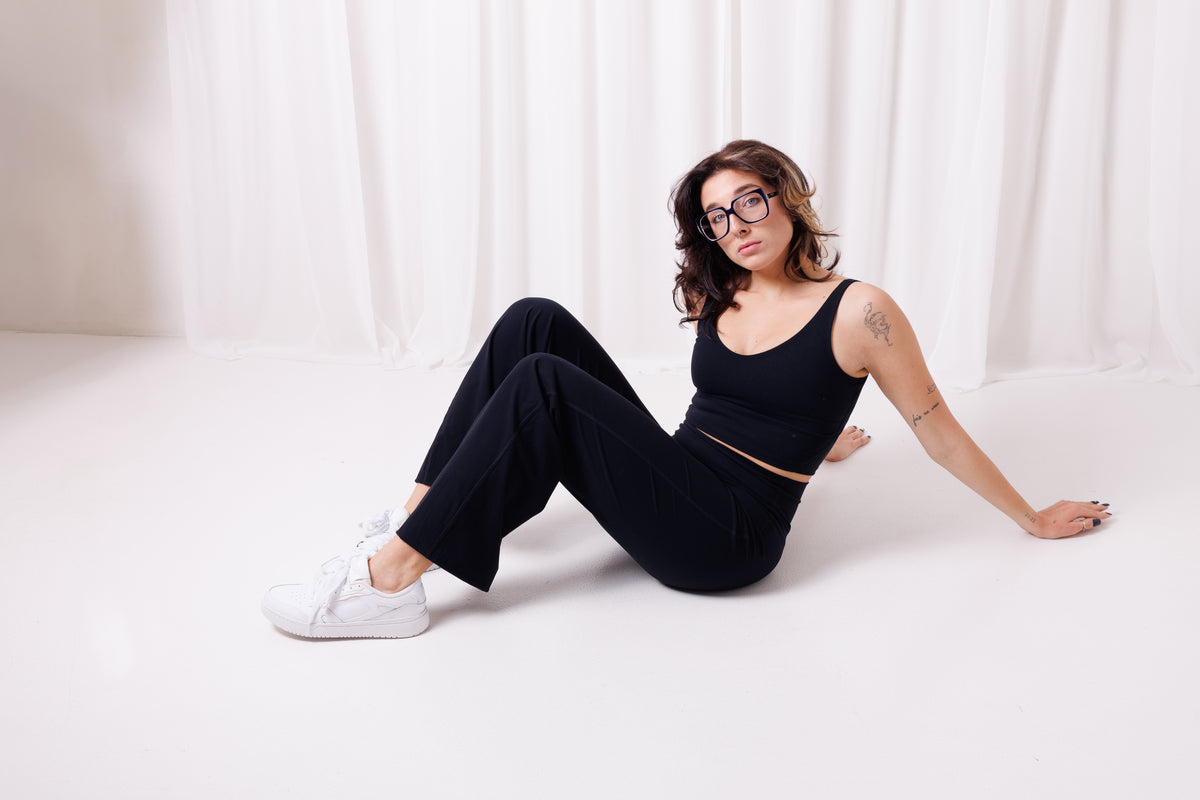 Modelka siedzi w spodniach Loose BalticBird z szerokimi nogawkami, czarny kolor, wygodne spodnie damskie z wysokim stanem, styl casual i sportowy